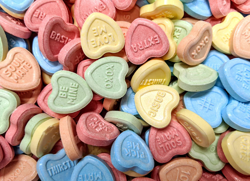Minonk Chocolate Company's Conversation Hearts - 8 oz. features colorful, heart-shaped candies in pink, yellow, green, orange, and blue with embossed phrases like LOVE ME, SOUL MATE, BE MINE, XOXO, and BASIC.